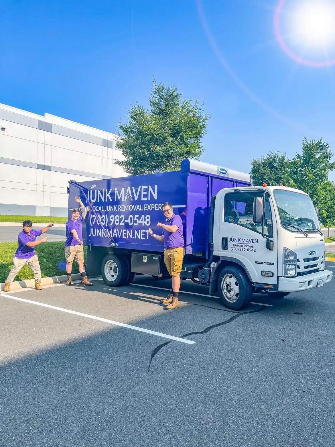 A joyful image showcasing three members of the Junk Maven team, including myself, all smiling and pointing proudly at our signature purple Junk Maven dump truck. We are dressed in professional attire, embodying the spirit of clutter conquerors dedicated to creating cleaner, brighter spaces in Northern Virginia. The truck in the background symbolizes our commitment to efficient and effective junk removal services.